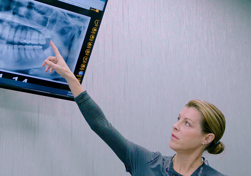 A staff member at Fioritto Family Dental pointing and a screen displaying digital x-rays of teeth.